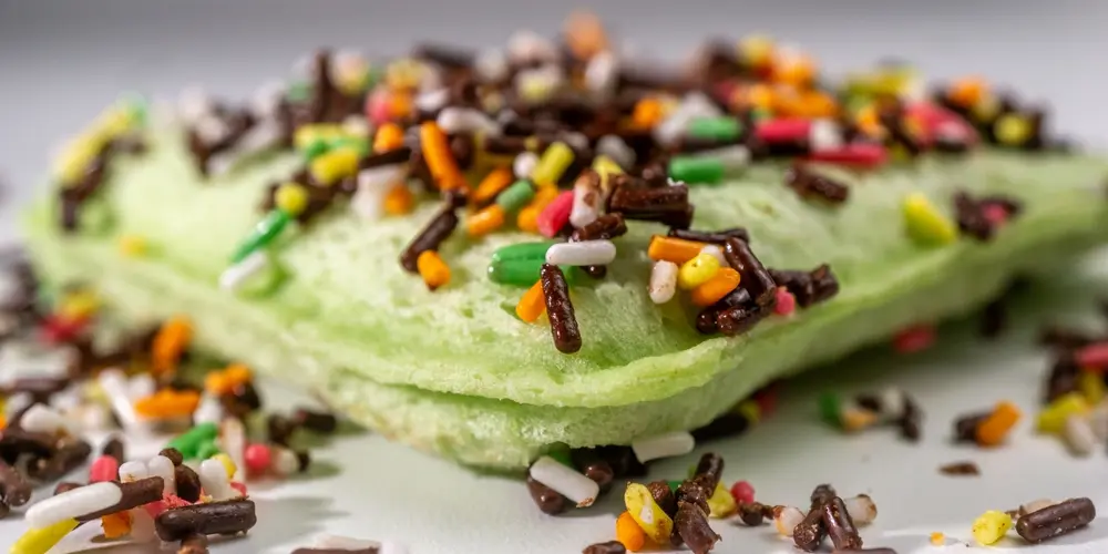 Gros plan sur un gâteau éponge vert recouvert de vermicelles colorés. Les vermicelles aux couleurs vives créent une ambiance ludique et festive qui contraste avec la douceur du gâteau.