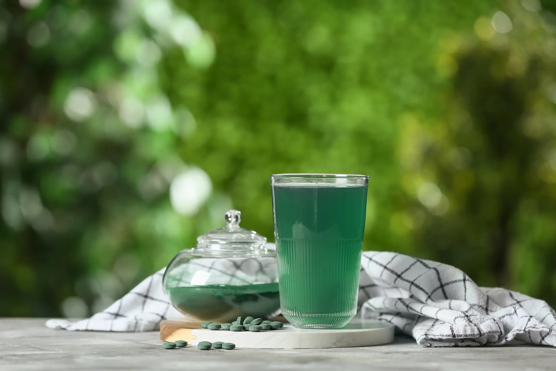 Jus vert dans un verre sur une table, entouré de plantes vertes.