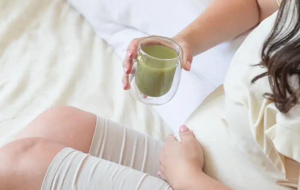 Femme enceinte boit de la spiruline verte saine, de l'ananas, de la banane et d'autres smoothies de fruits.