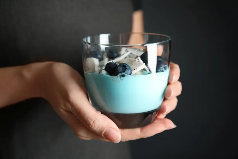 Femme tenant un verre de smoothie à la spiruline sur fond sombre, gros plan.