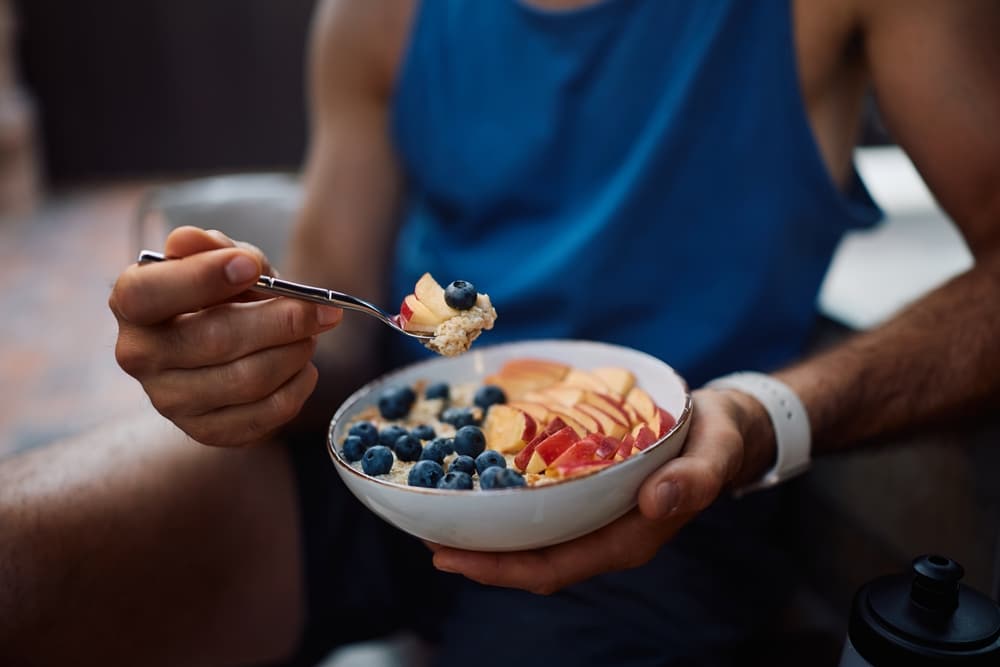 Close up of sportsman having healthy fruit oatmeal after exercise class.
