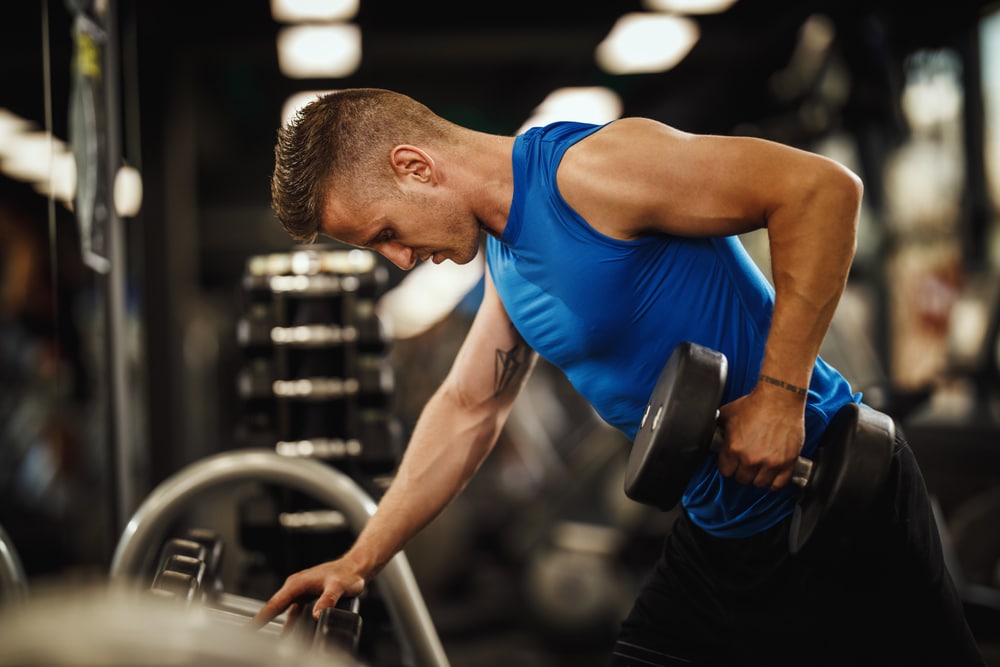 Plan d'un homme musclé en tenue de sport en plein entraînement intensif à la salle de sport. Il travaille les muscles de son dos avec des charges lourdes.