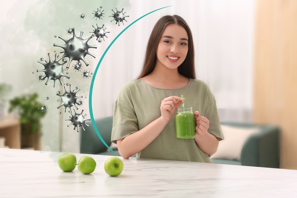 Une femme souriante, tenant un smoothie vert dans un bocal, est assise à une table auprès de trois pommes vertes. Des symboles de virus et une courbe dynamique suggèrent des bienfaits pour la santé.