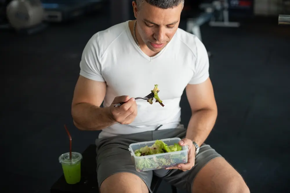 Homme mangeant de la salade en salle de sport.